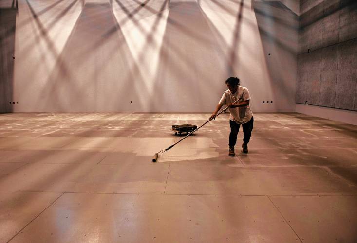 Merisa Dion, an employee at Wooden Kiwi, paints the floor of the Workroom, the largest performance space at 33 Hawley. 