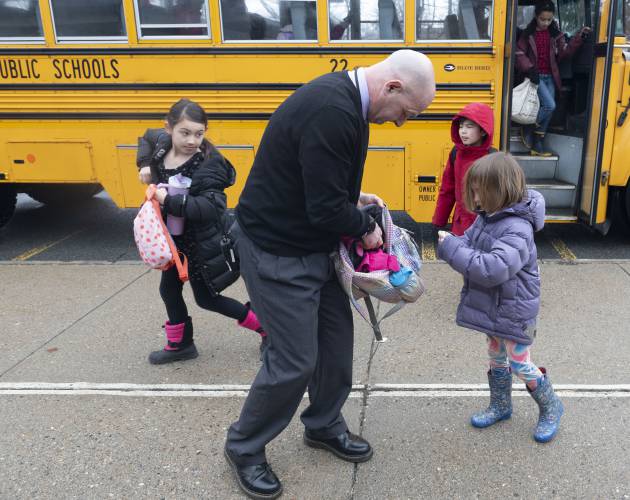 Derek Shea, principal at Crocker Farm Elementary School in Amherst, stops to help Simon Sandak repack her backpack as she gets off the bus as Kiera Thompson, left, and Taiga Takahash make their way to the school Wednesday morning. 